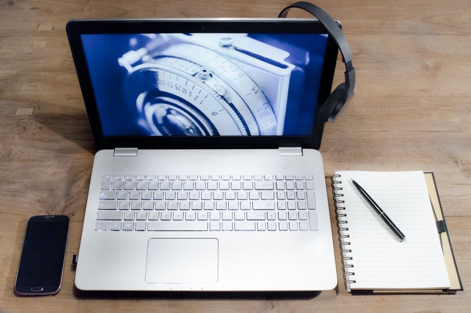 Top view of a modern workspace with a laptop, smartphone, headphones, and a notebook on a wooden desk.