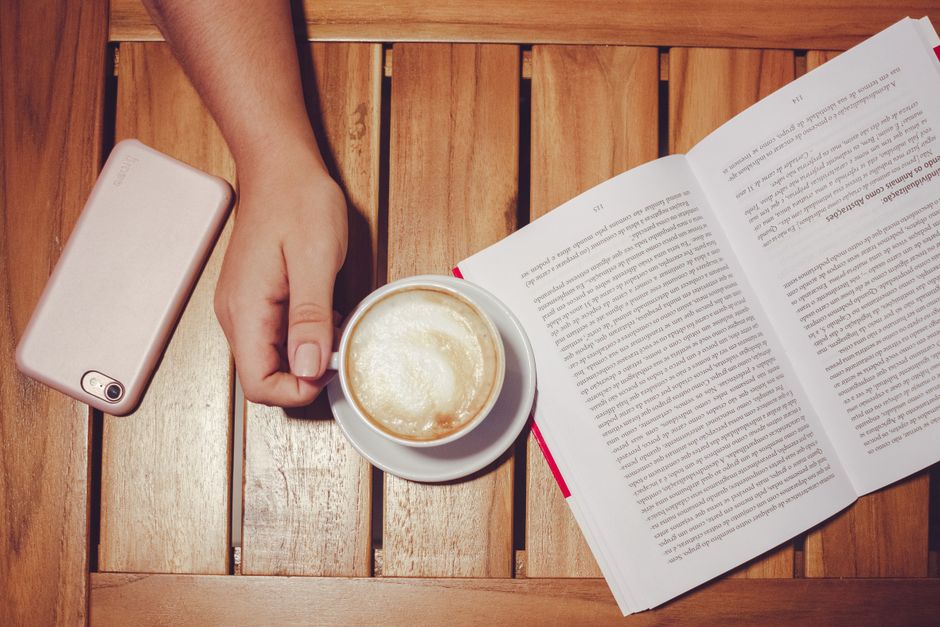 A peaceful scene featuring an open book, a cup of latte, and a smartphone on a wooden table.