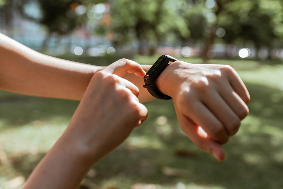 Crop faceless slim female tapping on fitness bracelet screen while training time in sunny summer park